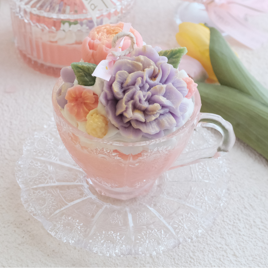 Miss Blooms Vintage Tea Cup Candle showing purple carnation and peach floral wax arrangement in glass teacup, garden background
