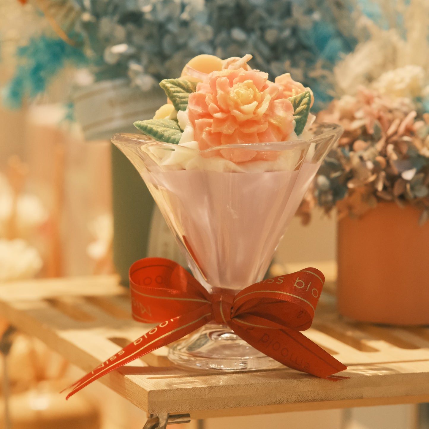 Miss Blooms Flower Cup Candle โ top-down view of coral peony and green leaf wax arrangement in cocktail glass