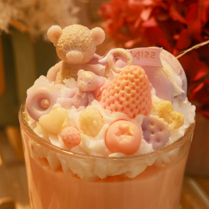 Miss Blooms Sweet Treats Giant Sundae Candle in tall cylindrical glass — sandy teddy bear and strawberry wax toppings in warm golden ambient light