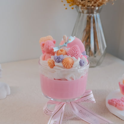 Miss Blooms Sweet Treats Giant Sundae Candle in pink footed glass jar with teddy bear, strawberry and berry wax toppings, Miss Blooms pink ribbon, dried yellow flowers in background
