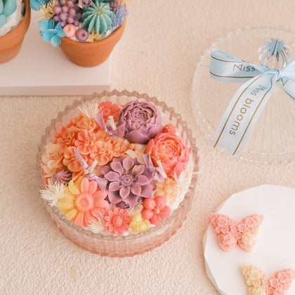 Miss Blooms Sunset Bloom Flower Candle from the side with dome lid and blue ribbon showing full candle height