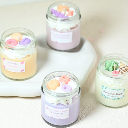 Miss Blooms Small Jar Candles in four fragrances on a white ceramic tray — each jar has pastel wax toppings including macarons, fruits and floral swirls